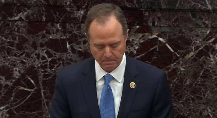 A man in a dark suit with a blue tie and congressional pin stands with his head bowed