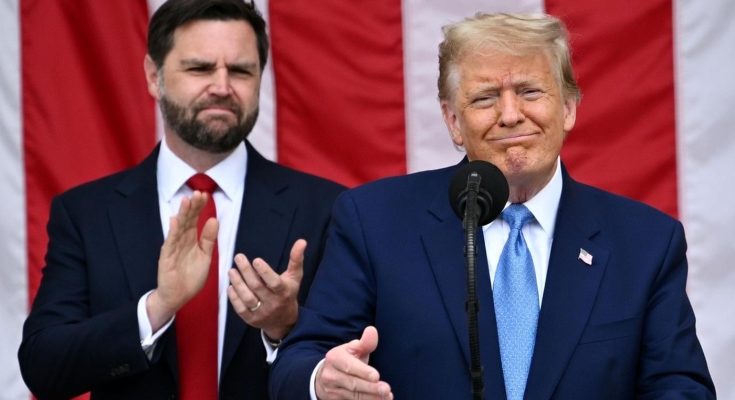 Donald Trump speaking at a podium with JD Vance clapping behind him, American flag