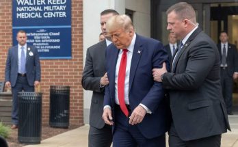 donald Trump in navy suit and red tie escorted by Secret Service agents outside Walter