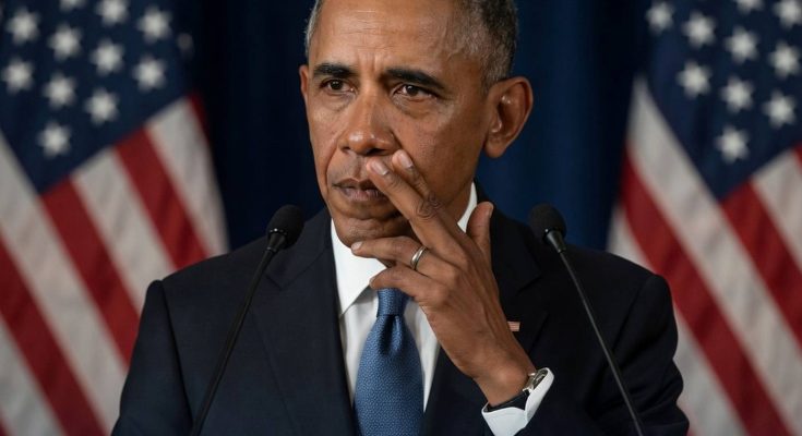 barack Obama speaking at podium with American flags behind, touching face with concerned
