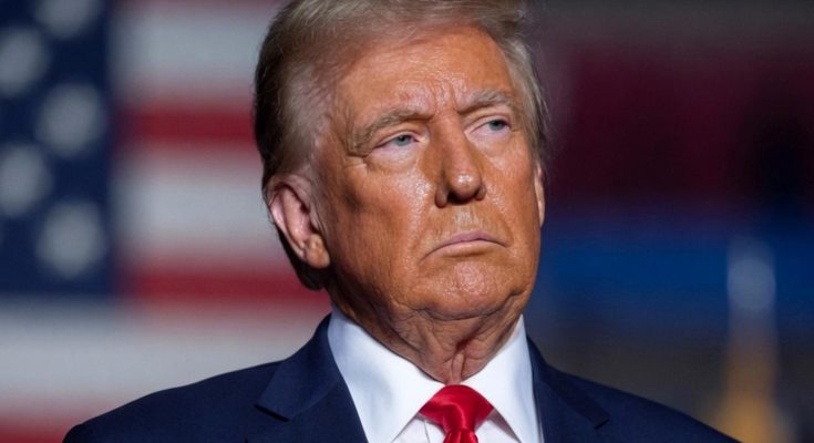 donald Trump in navy suit with red tie stands before American flag with Emergency News