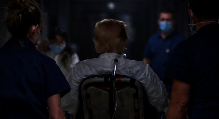 patient in wheelchair escorted by medical staff in dim hallway