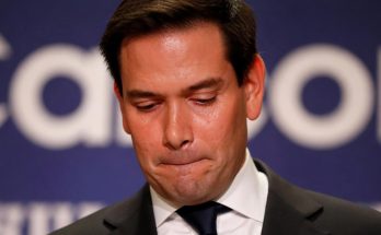 man in suit looking down, appearing contemplative at a conference