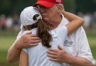 man in red hat embraces young girl on golf course