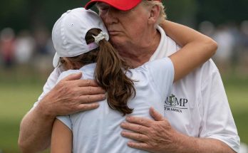 man in red hat embraces young girl on golf course