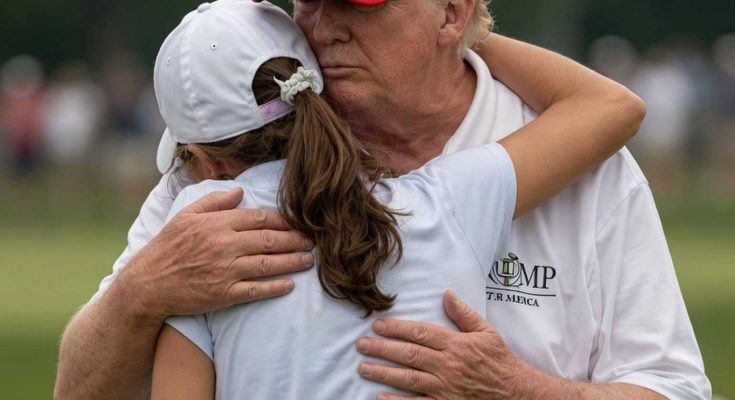 man in red hat embraces young girl on golf course