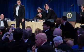security personnel assist man at formal event with presidential seal