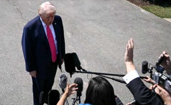 donald Trump in navy suit and red tie speaking to reporters with microphones and cameras