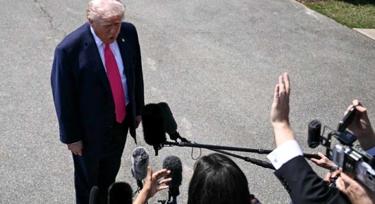 donald Trump in navy suit and red tie speaking to reporters with microphones and cameras