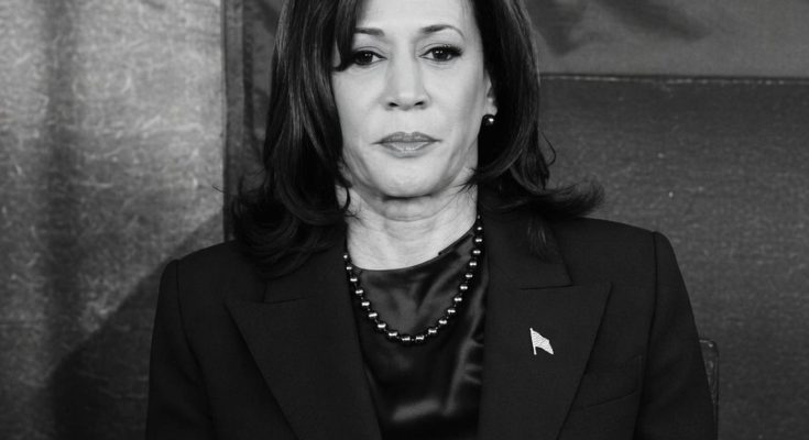 woman in dark suit with flag pin and necklace, solemn expression