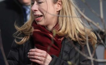chelsea Clinton wearing a burgundy scarf and black quilted coat, holding a phone, with