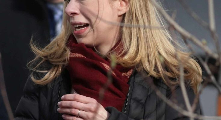 chelsea Clinton wearing a burgundy scarf and black quilted coat, holding a phone, with