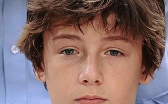 close-up portrait of a teenage boy with tousled brown hair and freckles, wearing a