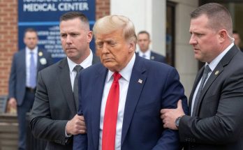 donald Trump in navy suit and red tie being escorted by two Secret Service agents outside