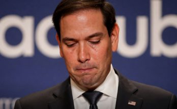marco Rubio with tears streaming down his face at a podium with breaking news banner