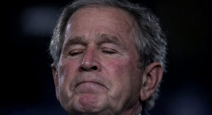 george W. Bush with eyes closed and somber expression against dark background with yellow