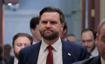 vice President JD Vance walks through Capitol hallway wearing navy suit and red tie after