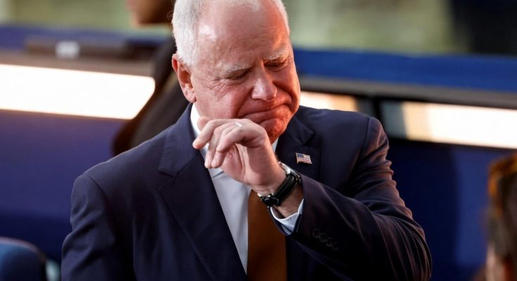 tim Walz seated with eyes closed, hand raised to his face, wearing navy suit and American
