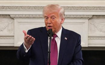 man in suit speaking at microphone in formal setting