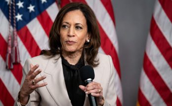 woman in suit speaking with American flags in background