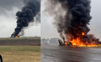 aircraft wreckage engulfed in flames on wet runway with massive black smoke plume rising