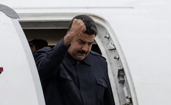 nicolas Maduro raising fist while exiting airplane doorway in dark military-style uniform