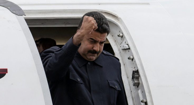 nicolas Maduro raising fist while exiting airplane doorway in dark military-style uniform