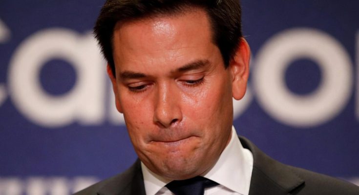 man in suit looking down, serious expression, blue background