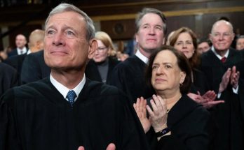 chief Justice John Roberts and Supreme Court justices applauding in black robes with