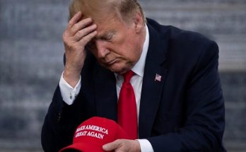 man in suit holding red cap, looking contemplative