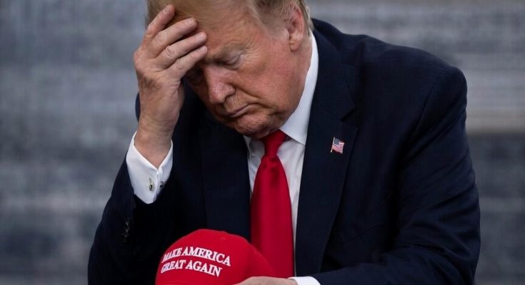 man in suit holding red cap, looking contemplative