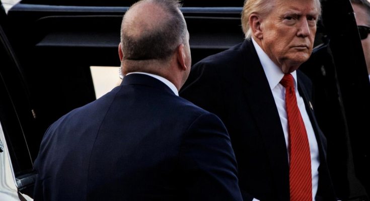 donald Trump wearing dark suit and red tie exits vehicle with Secret Service agent nearby