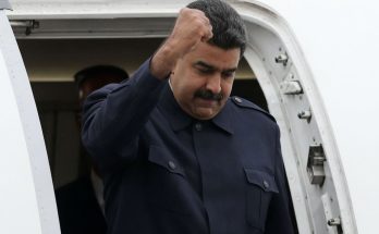 leader exits plane with raised fist in defiant gesture