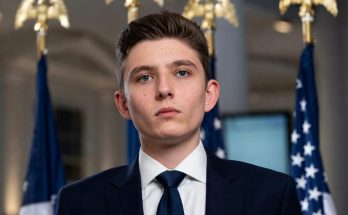 young man in suit with flags in background, serious expression