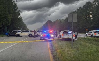 sheriff vehicles with flashing lights block rural highway under storm clouds with yellow