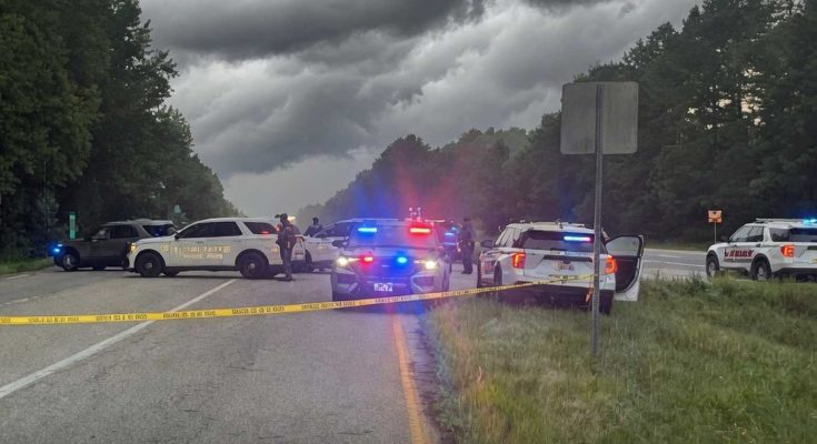 sheriff vehicles with flashing lights block rural highway under storm clouds with yellow