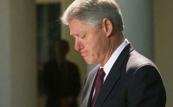 president Bill Clinton with head bowed and hands clasped during a solemn outdoor moment