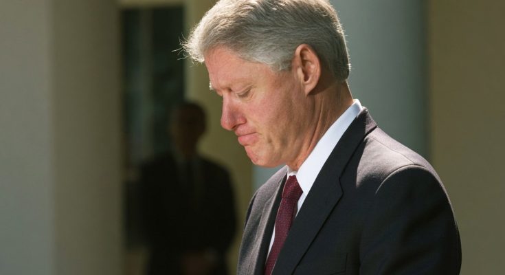 president Bill Clinton with head bowed and hands clasped during a solemn outdoor moment