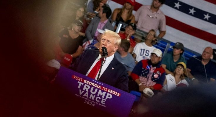donald Trump speaking at a rally with crowd and US flag