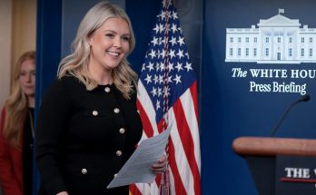 smiling woman holding papers at White House press briefing