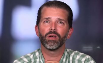 donald Trump Jr speaking during television interview with hands clasped wearing green