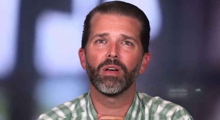 donald Trump Jr speaking during television interview with hands clasped wearing green