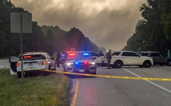 police vehicles with flashing lights block a rural highway under stormy skies, yellow