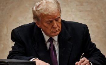 man in suit writing at desk with focused expression