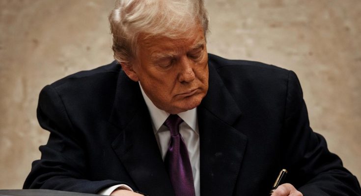 man in suit writing at desk with focused expression