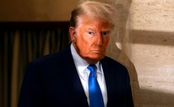 donald Trump in dark navy suit and bright blue tie standing beside travertine wall with