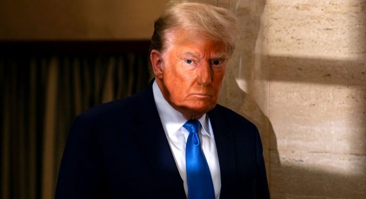 donald Trump in dark navy suit and bright blue tie standing beside travertine wall with