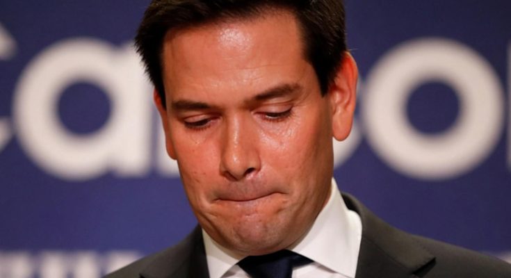 marco Rubio looking down with eyes closed at political event with Breaking News banner