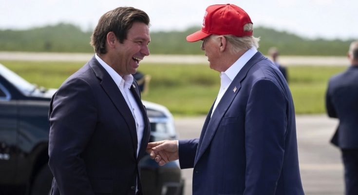 donald Trump in red MAGA cap shakes hands with Ron DeSantis on airport tarmac with black