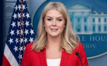 karoline Leavitt at White House press briefing podium wearing red blazer, American flag